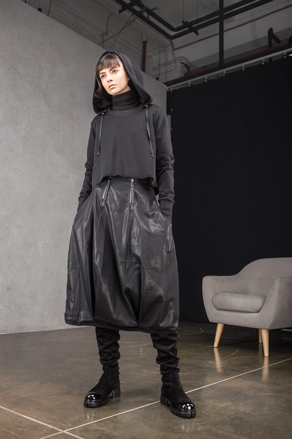 Person wearing a dark outfit with a hood in an indoor setting