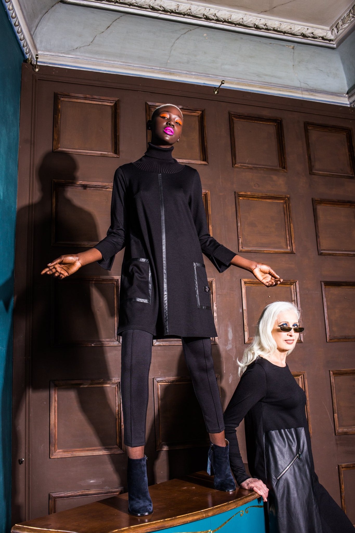 Two women in black outfits standing in a room with wooden paneling. Japanese fabric 