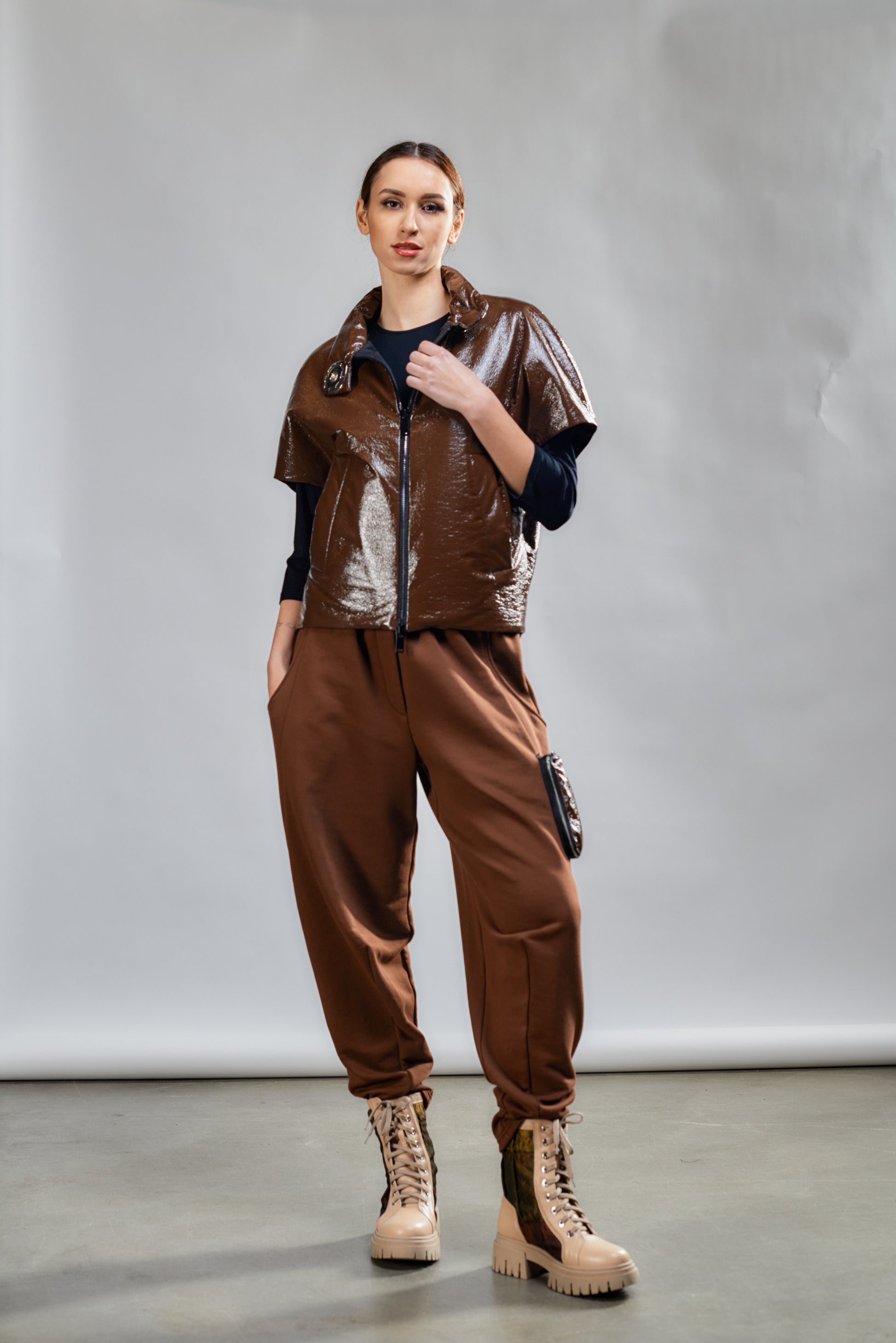 Person wearing a brown outfit with a metallic vest against a plain background