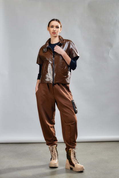 Person wearing a brown outfit with a metallic vest against a plain background
