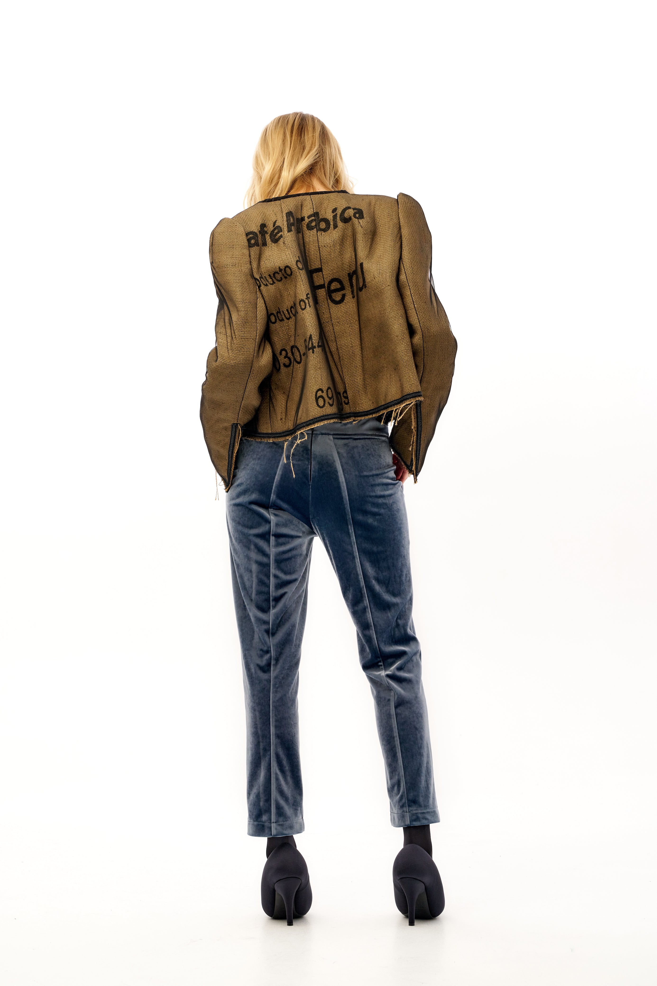 Person wearing a brown jacket with text and blue jeans on a white background